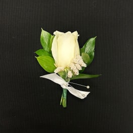 White rose boutonniere with green leaves and a white ribbon