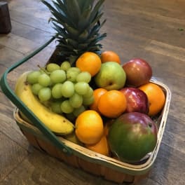 Basket of assorted fruit with a pineapple, grapes, bananas, oranges, apples, and a pear