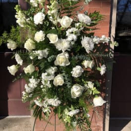 Tall standing spray of white roses, carnations, and other flowers on a metal easel