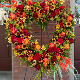 Large floral wreath with red, orange, and yellow blooms on a black stand