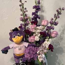 Purple floral arrangement with a Rockies mascot plush in a vase