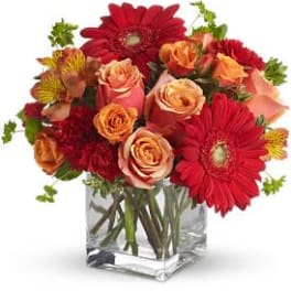 Bouquet of red gerbera daisies and peach roses in a clear glass vase