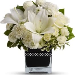 White lilies and roses arranged in a clear square vase with a black ribbon