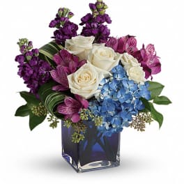 Bouquet of white roses, blue hydrangeas, and purple flowers in a blue glass vase