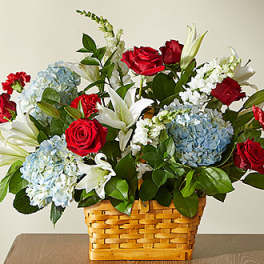 Basket arrangement of red roses, blue hydrangeas, and white lilies