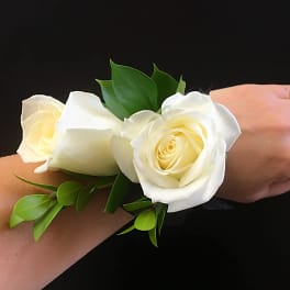 White rose wrist corsage with green leaves on a black ribbon