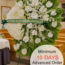 Tall white sympathy standing spray with clustered white flowers and glossy green leaves on an easel.