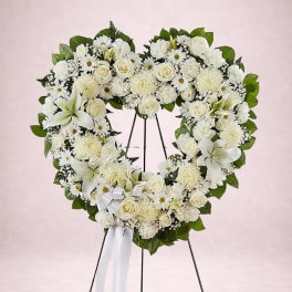 Heart-shaped white floral wreath on a stand with a ribbon bow
