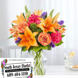 Bouquet of orange lilies, peach roses, and pink carnations in a glass vase