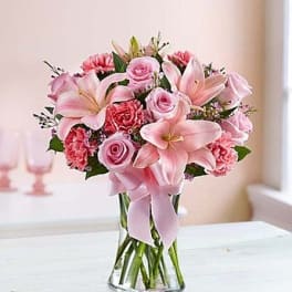 Pink roses and lilies arranged in a clear glass vase with a ribbon