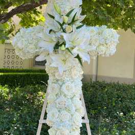White floral cross on a wooden easel with roses and lilies