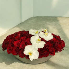 Low arrangement of red roses with white orchids in a shallow gray container