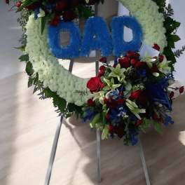 Floral funeral wreath with blue "DAD" lettering on a stand