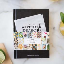 A cookbook on a marble surface with glasses of drink around it
