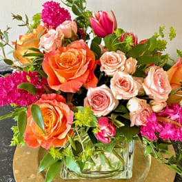 Mixed bouquet of orange and blush roses with pink blooms in a glass vase.