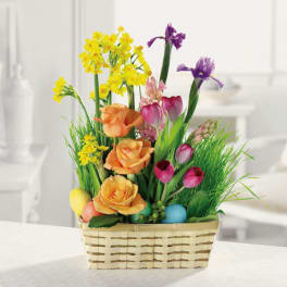 Basket arrangement with yellow, orange, pink, and purple spring flowers and colorful Easter eggs