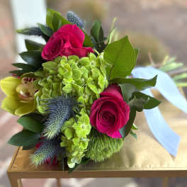 Hand-tied bouquet with hot pink roses, green hydrangea, yellow orchid and blue thistle tied with a blue ribbon