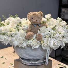 White rose arrangement with a teddy bear in a gray bowl vase