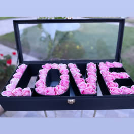 Pink roses arranged to spell LOVE in a black box