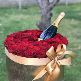 Red roses arranged in a round box with a champagne bottle and gold ribbon