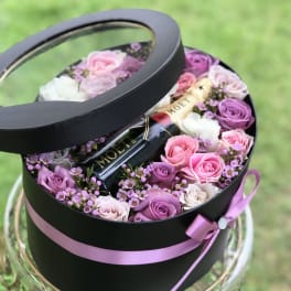Round black gift box with pink and purple roses and a champagne bottle