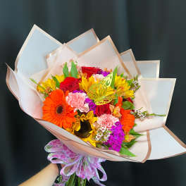 Colorful bouquet with roses, gerbera daisies, and carnations wrapped in pale paper