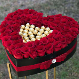 Heart-shaped box of red roses with gold-wrapped chocolates in the center