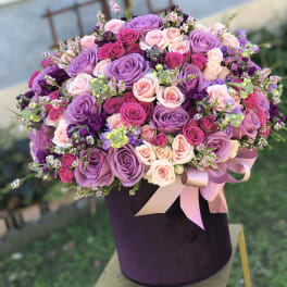 Large bouquet of pink and purple roses in a dark hat box with ribbon