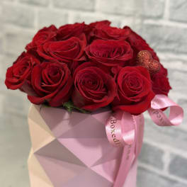 Red roses arranged in a pink geometric box with a ribbon