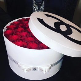 Round white box filled with red roses and a lid with a black logo