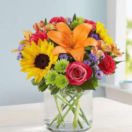 Bright mixed bouquet with sunflowers, orange lily, pink rose, and colorful blooms in a clear glass vase