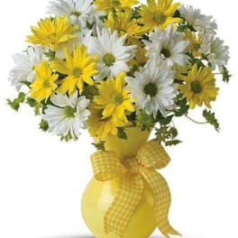 Yellow and white daisy bouquet in a yellow vase with a ribbon