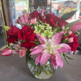 Round glass vase arrangement with red roses, pink lilies, tulips, and green hydrangea