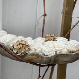 White roses arranged in a shallow wooden vessel with dried accents