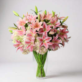 Pink lilies and hydrangeas arranged in a clear glass vase
