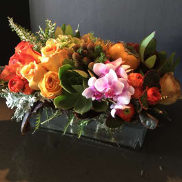 Orange roses and pink orchids in a low rectangular vase