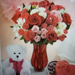 Red and white rose bouquet in a red vase with a teddy bear and chocolates