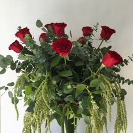 Tall bouquet of red roses with cascading green foliage in a glass vase