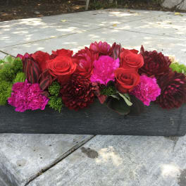 Low rectangular arrangement of red and pink flowers in a dark planter