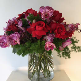 Red roses and pink orchids arranged in a glass vase