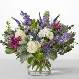Mixed bouquet of white roses, purple flowers, and blue thistles in a glass vase