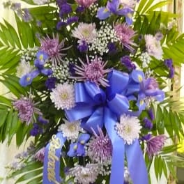 Purple and white funeral spray with a blue ribbon and palm fronds