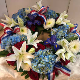 Floral wreath with blue hydrangeas, white lilies, red roses, and ribbon bows