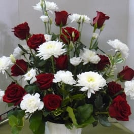 Red roses and white daisies arranged in a white bucket vase