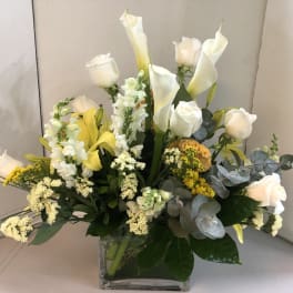 White roses and calla lilies arranged in a clear square vase