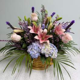Basket arrangement with pink lilies, roses, and blue hydrangeas