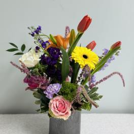 Mixed bouquet in a gray vase with tulips, roses, and a yellow gerbera daisy