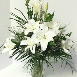 White lilies arranged in a clear glass vase with greenery