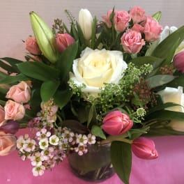 Compact arrangement of white roses, pink spray roses, and tulips in a clear glass vase