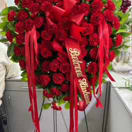Heart-shaped standing spray of red carnations with ribbon